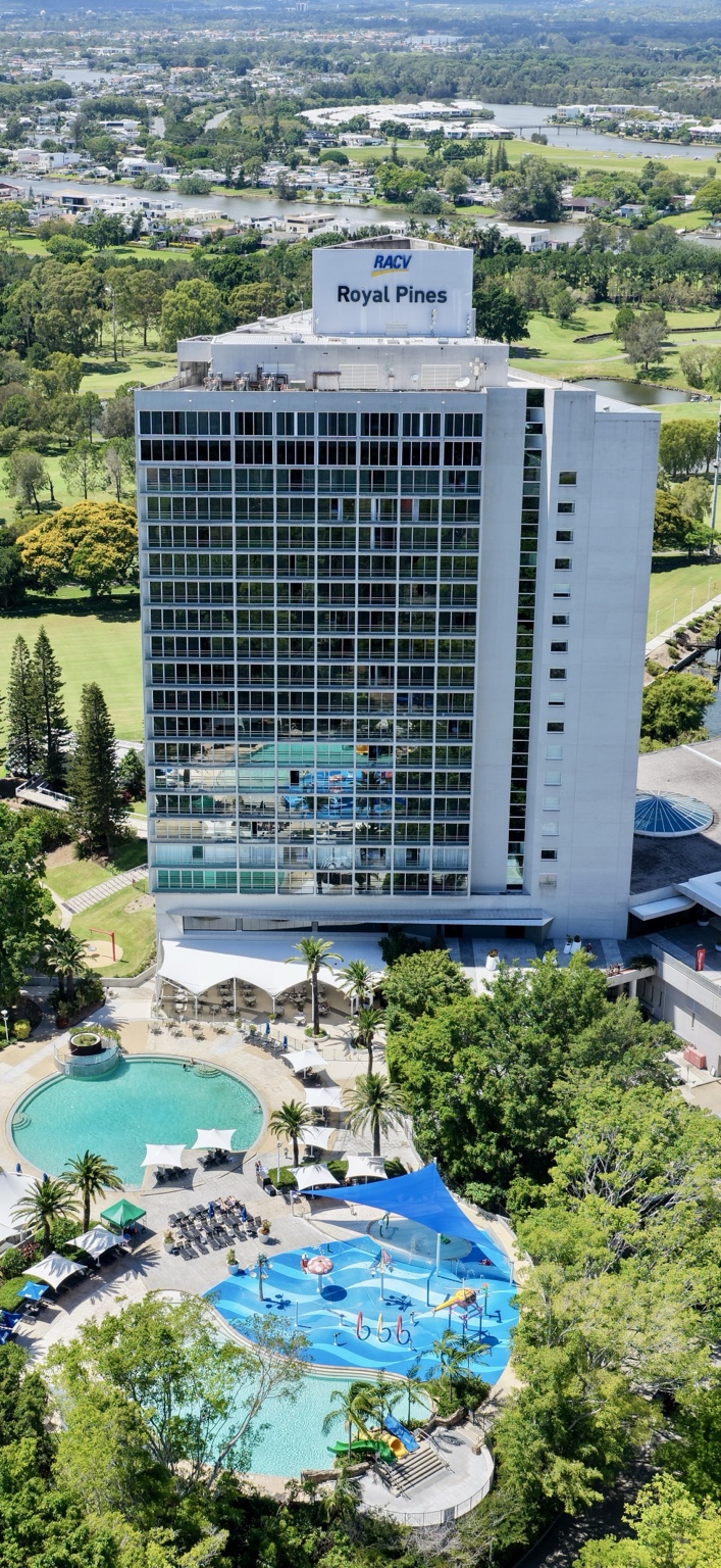 Vertical aerial view of RACV Royal Pines Resort tower, pools and landscaped resort grounds.