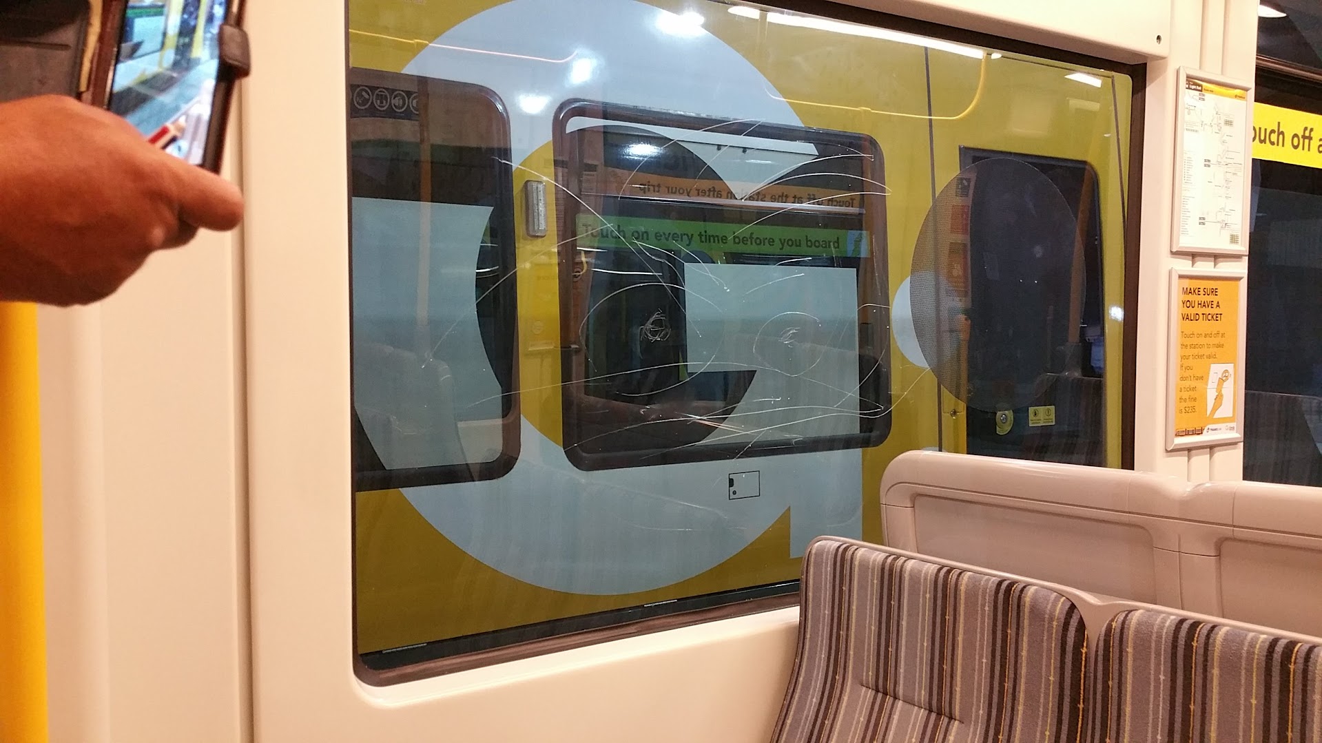 Scratched tram window showing sacrificial anti-graffiti film protecting transport glass.